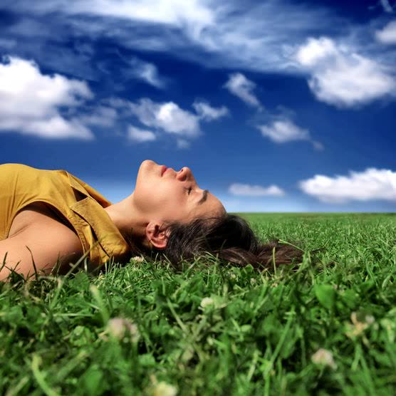 Eine Frau liegt im Gras, das Gesicht zum hellen Himmel, die Augen geschlossen.